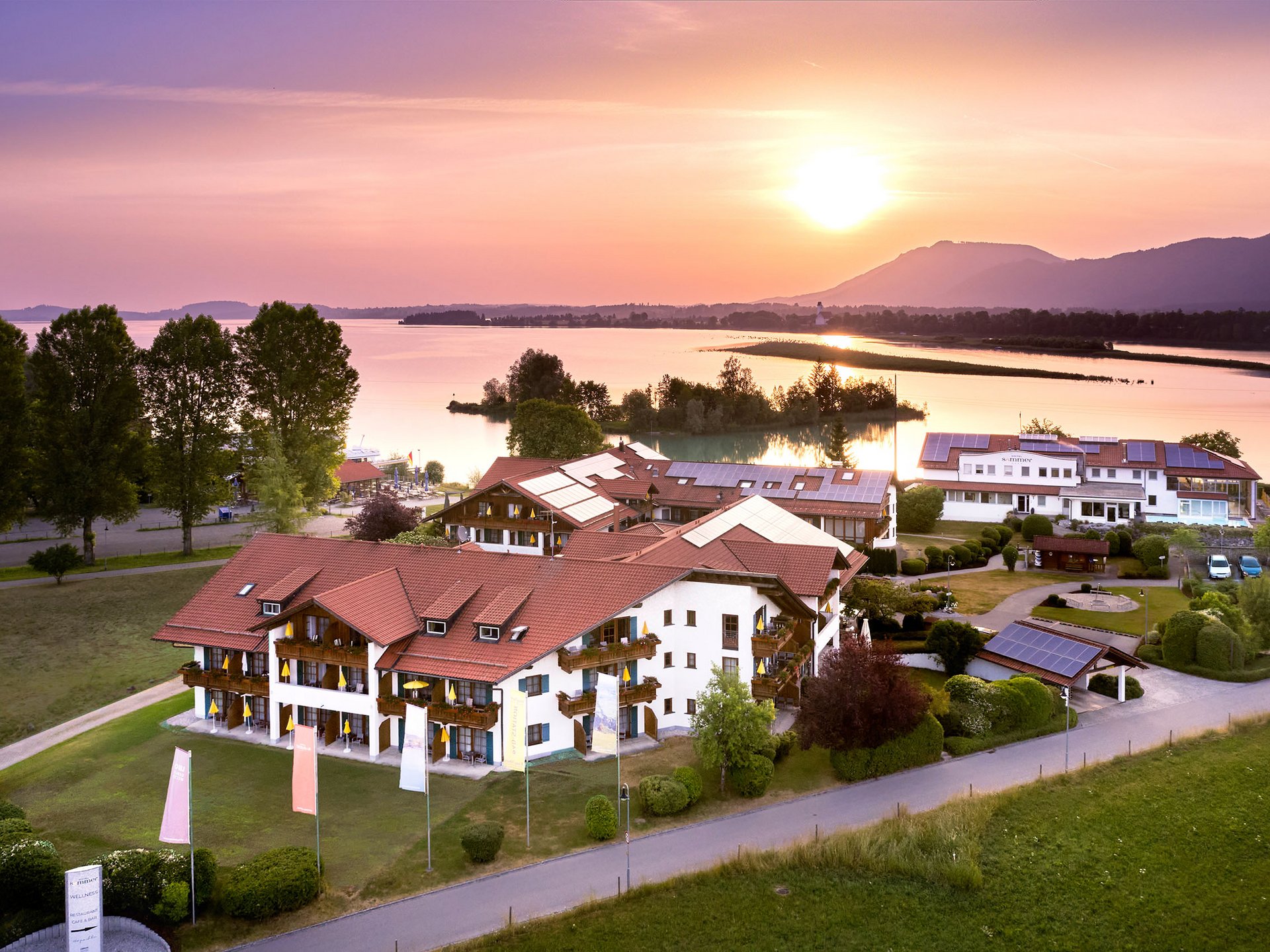 Hotelgebäude mit roten Dächern am Seeufer bei Sonnenuntergang
