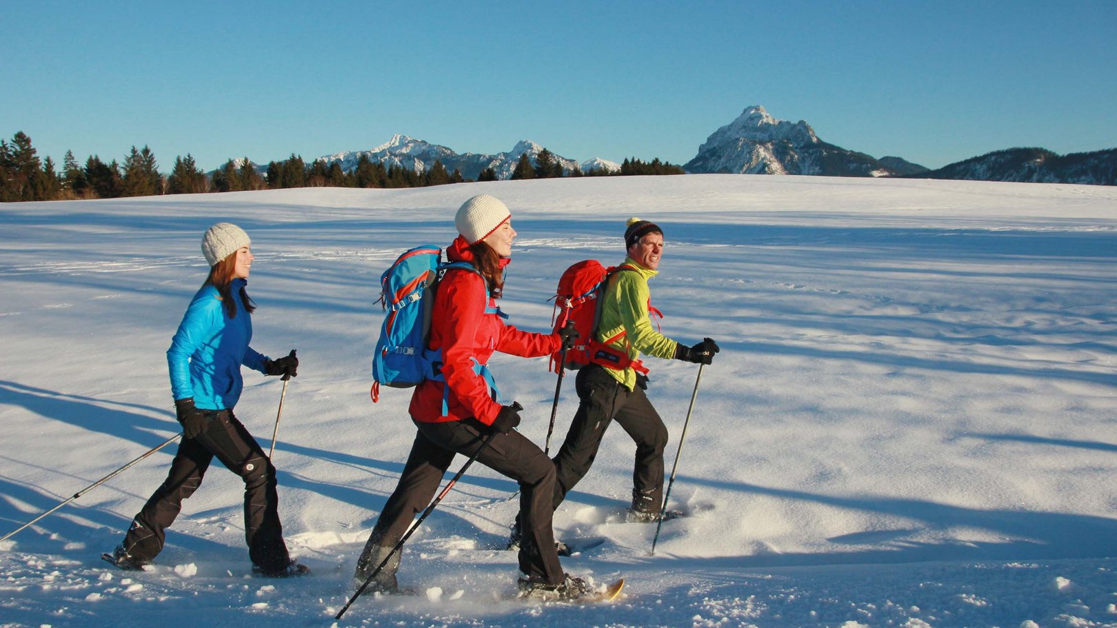 Winteraktivitäten rund um das Hotel Sommer Drei Personen beim Schneeschuhwandern auf verschneiter Fläche mit Bergen im Hintergrund