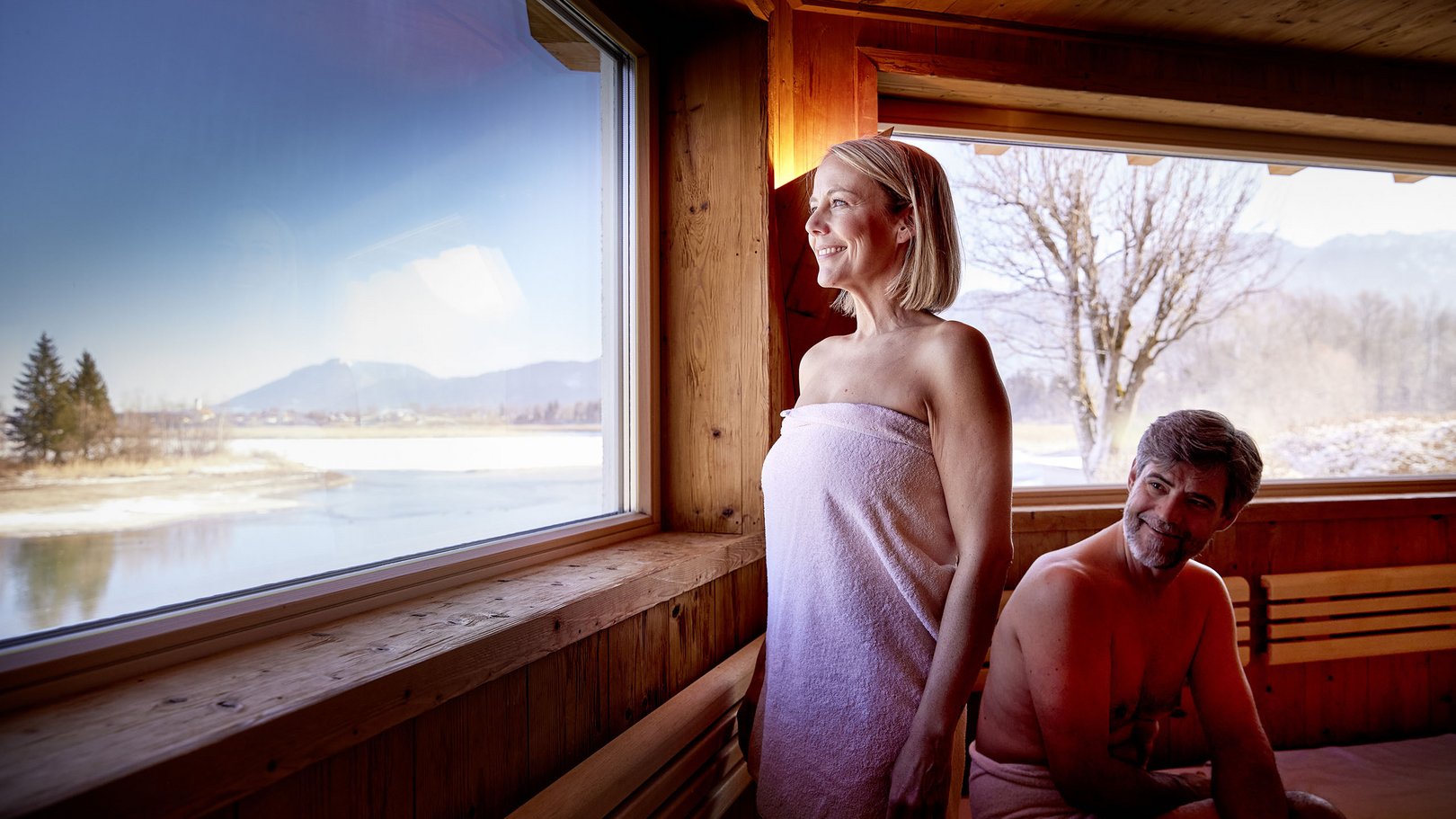 Skifahren im Allgäu | Hotel Sommer Füssen Frau und Mann in Sauna mit Blick auf verschneite Landschaft durch Fenster