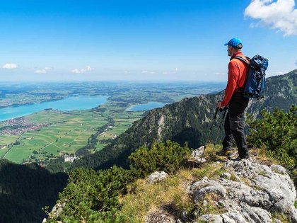 Segeln am Forggensee | Hotel Sommer Wanderer mit Rucksack blickt auf Tal und See von Berggipfel