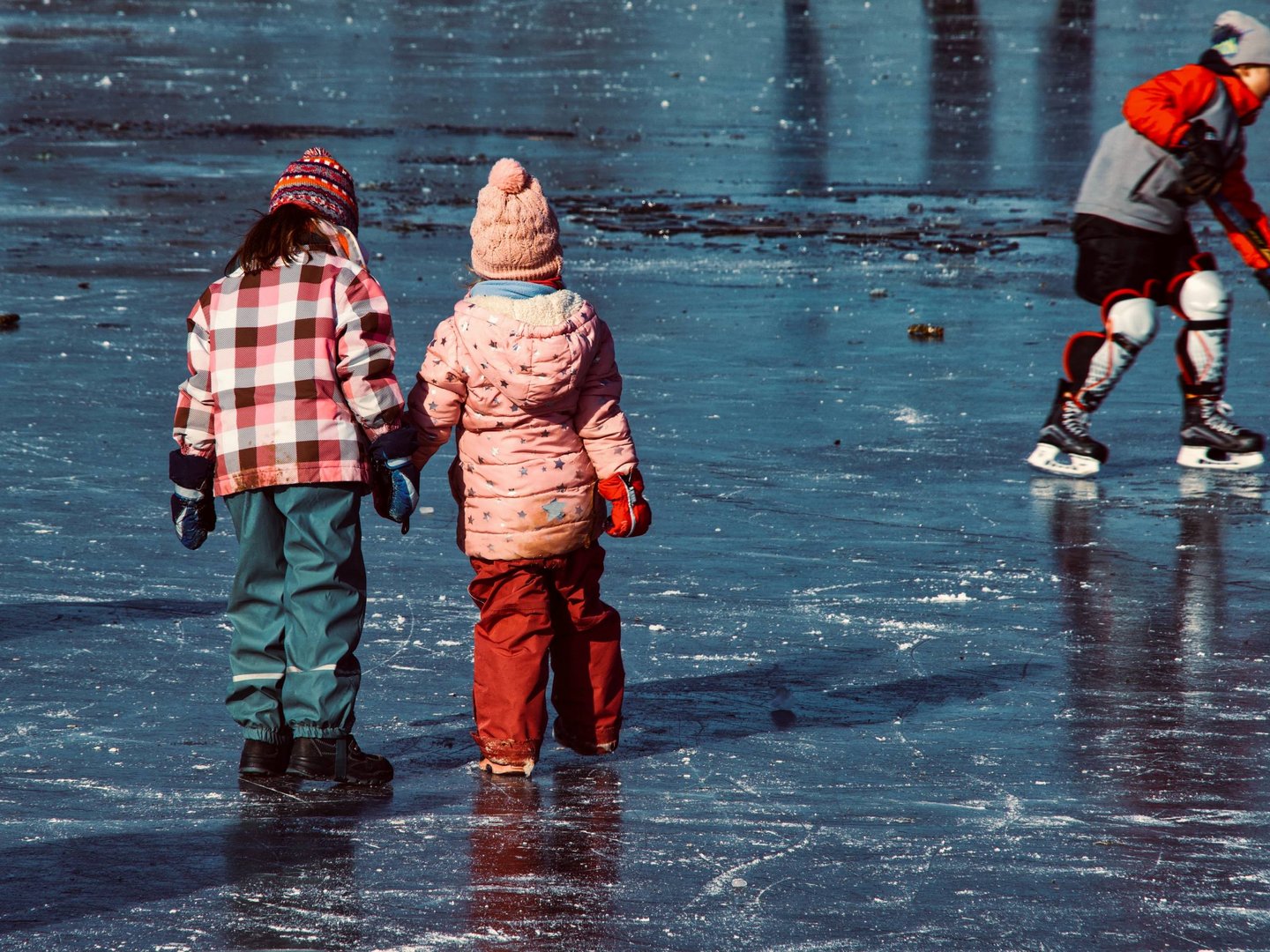 Winteraktivitäten rund um das Hotel Sommer Zwei Kinder halten sich beim Schlittschuhlaufen auf zugefrorenem See an der Hand